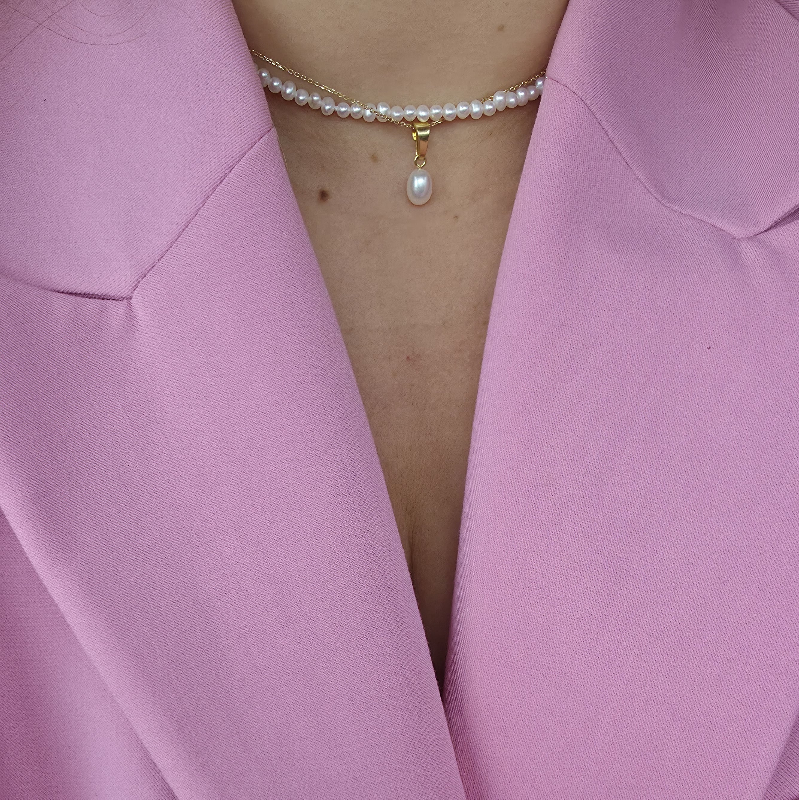Close-up of a pink blazer with a pearl necklace worn underneath.