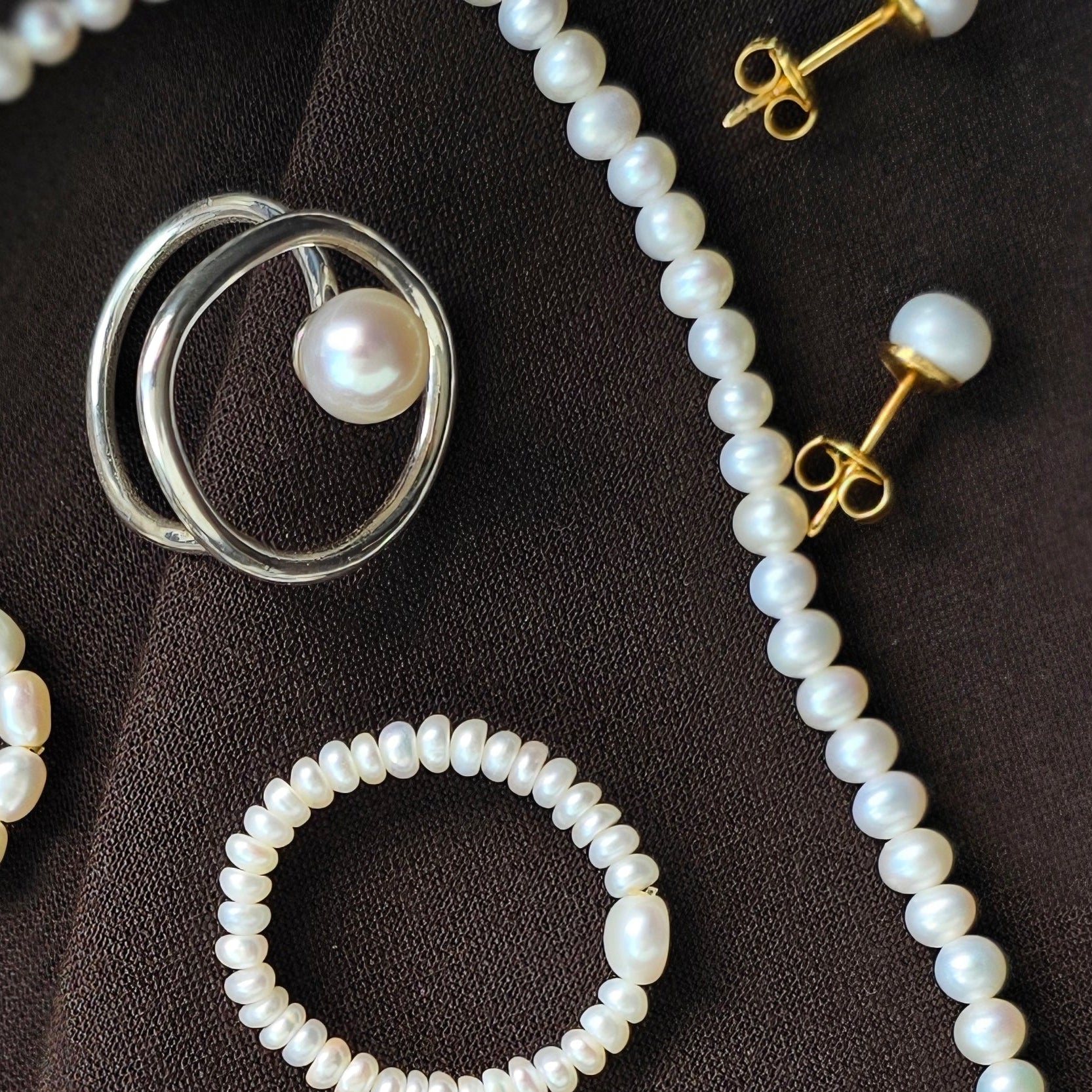 Pearl jewelry including a necklace, bracelet, and earrings on a dark surface.