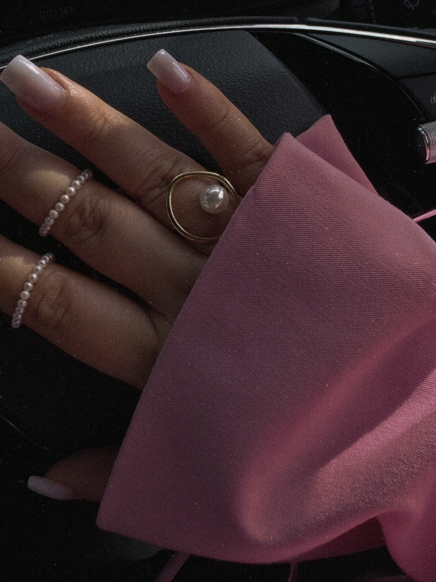Close-up of a hand with multiple pearl rings on a dark background