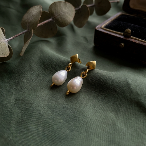 Gold earrings with pearls on a green fabric background