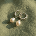 Silver hoop earrings with pearl drops on a green fabric background