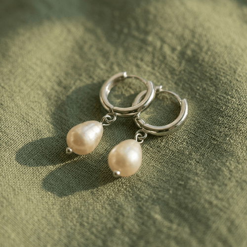 Silver hoop earrings with pearl drops on a green fabric background