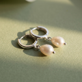 Silver hoop earrings with pearls on a light green surface