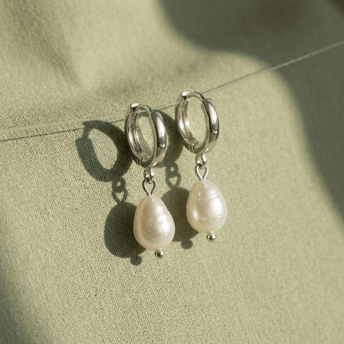 Silver hoop earrings with pearl drops on a green fabric background