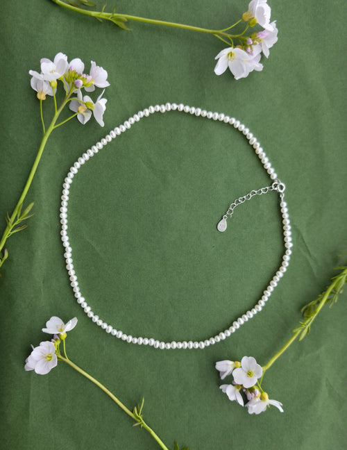 The Anna Necklace featuring natural freshwater pearls on a green background with delicate flowers.
