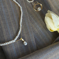 Pearl necklace, bracelet, and ring on a textured surface with a white flower.