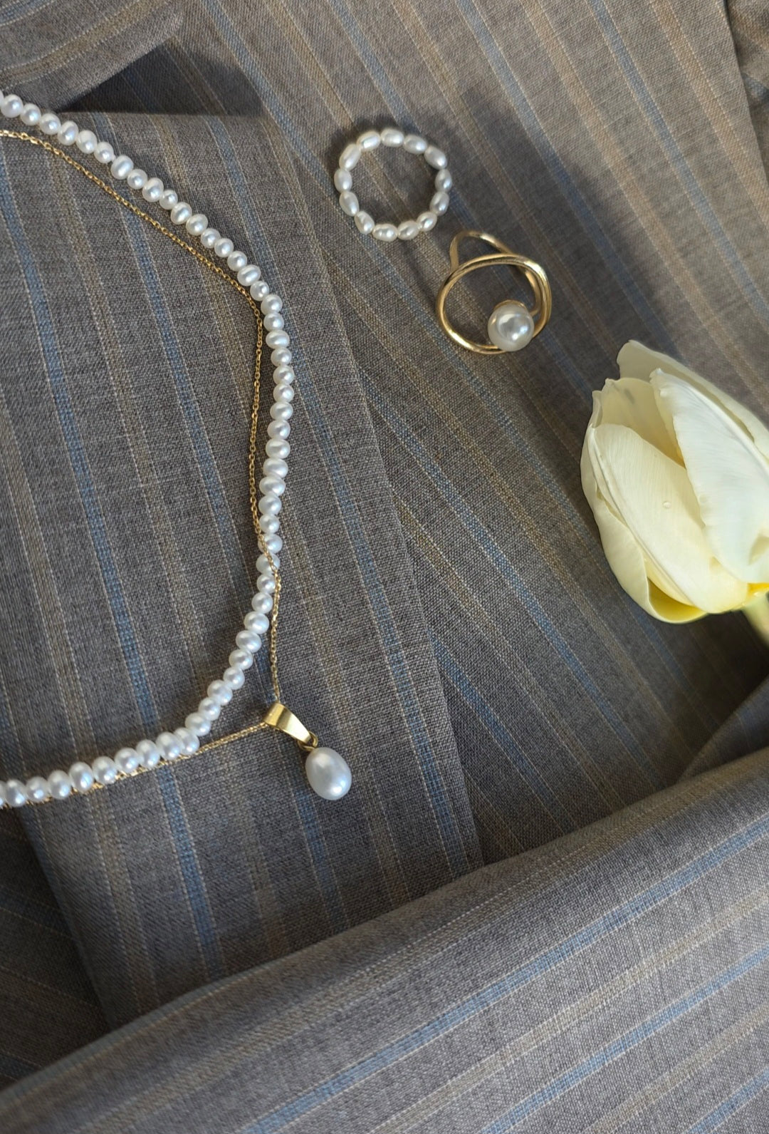 Pearl necklace, bracelet, and ring on a textured surface with a white flower.