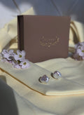 Pearl silver earrings on a light fabric surface with a brown box and small flowers.