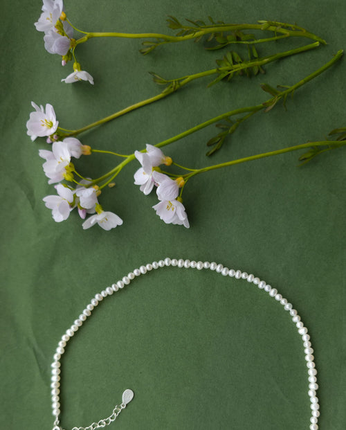 The Anna Necklace with natural freshwater pearls on green background with delicate flowers.