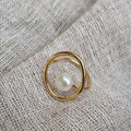 A pearl ring with an open silhouette on a textured background.