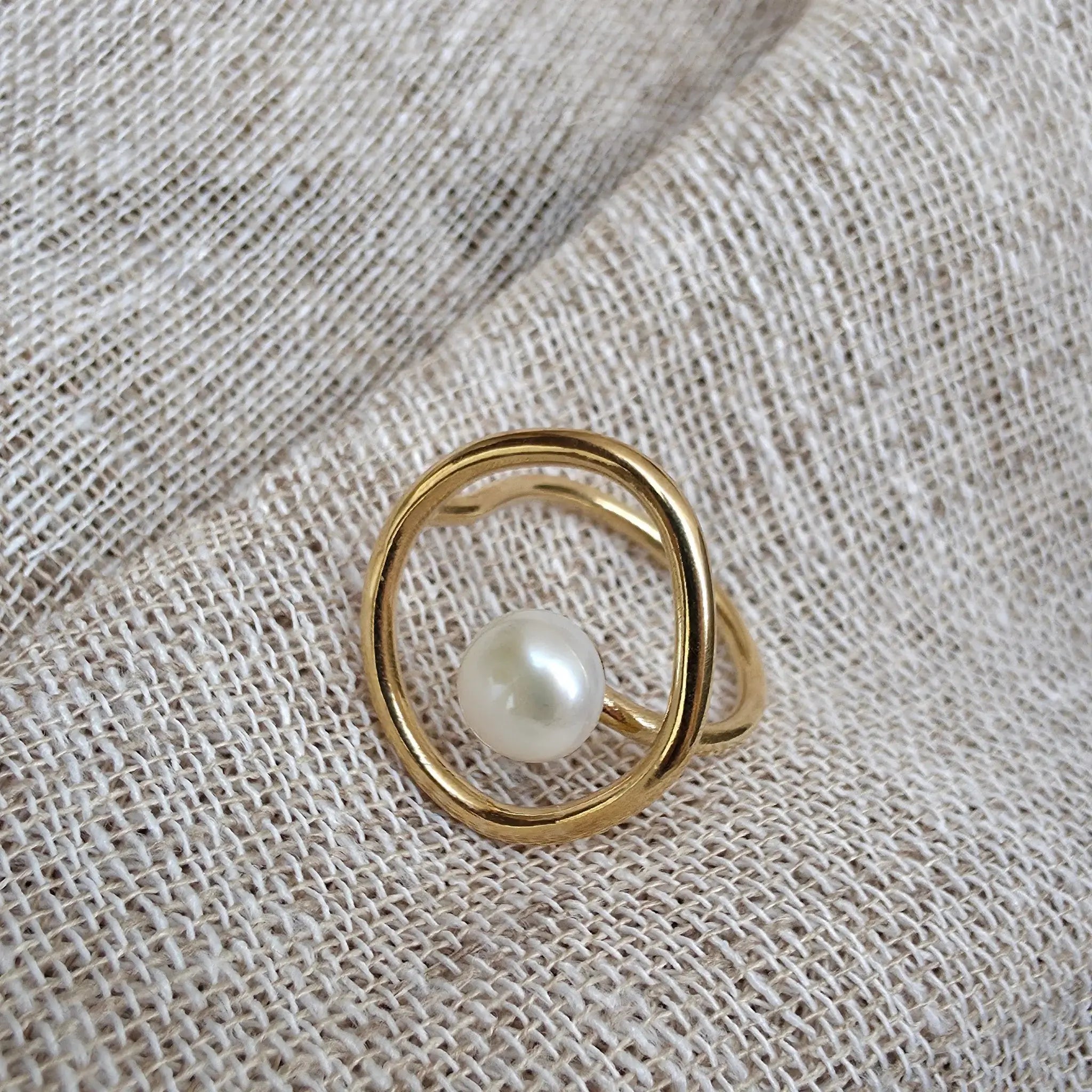 A pearl ring with an open silhouette on a textured background.