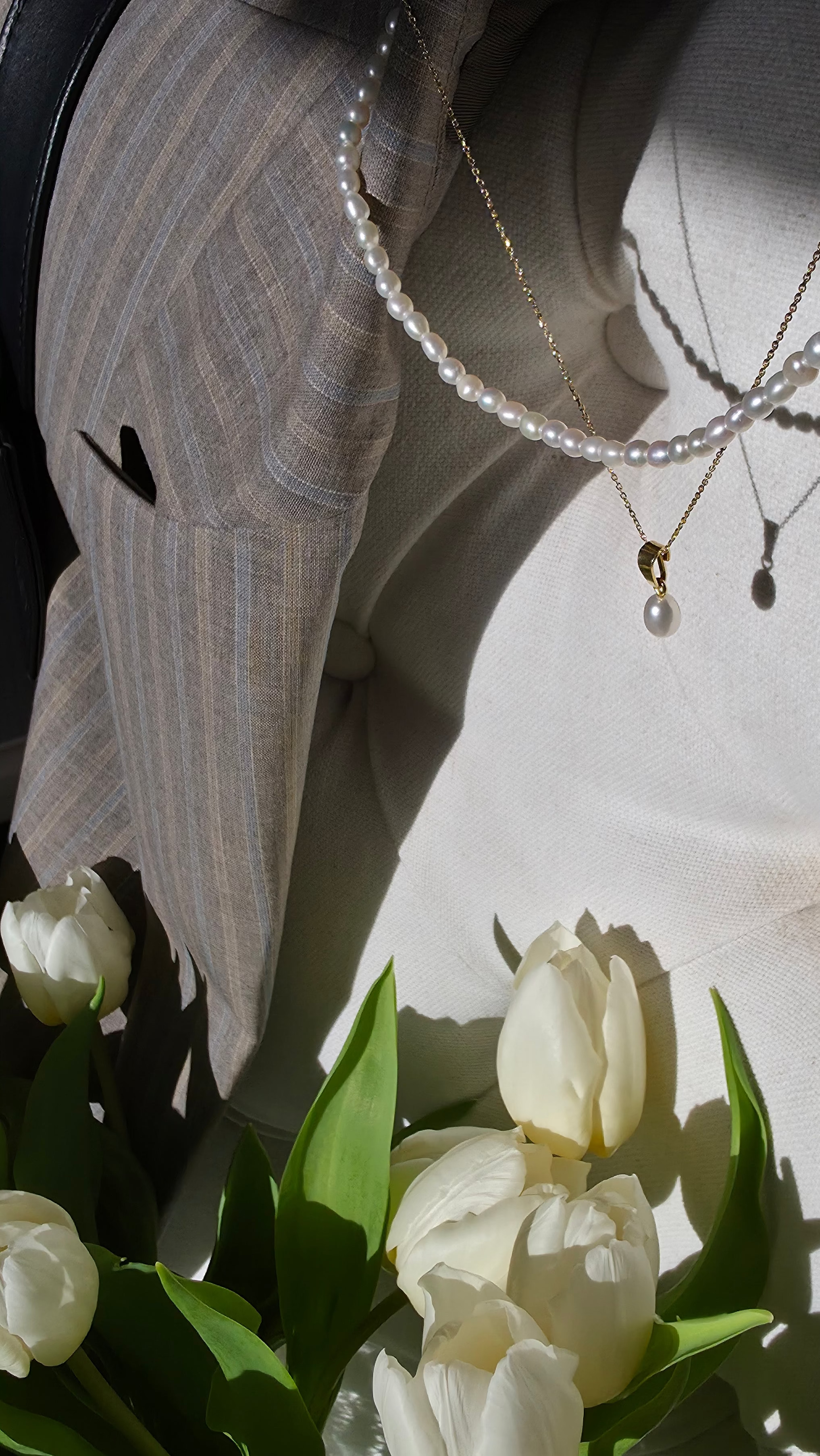 Close-up of a person wearing pearl necklaces with a bouquet of white tulips in the foreground.