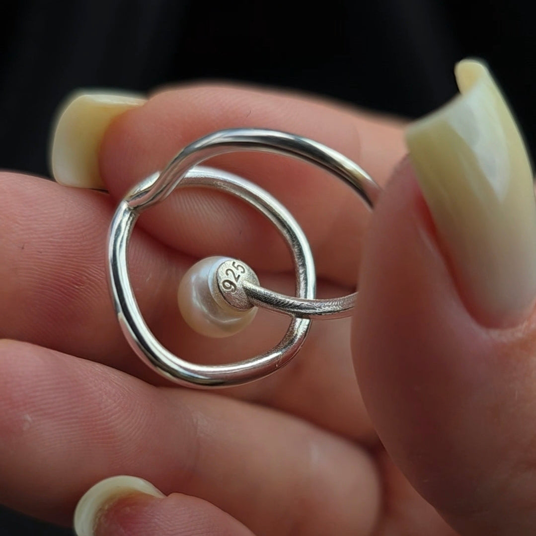 Silver ring with a pearl held between fingers against a dark background