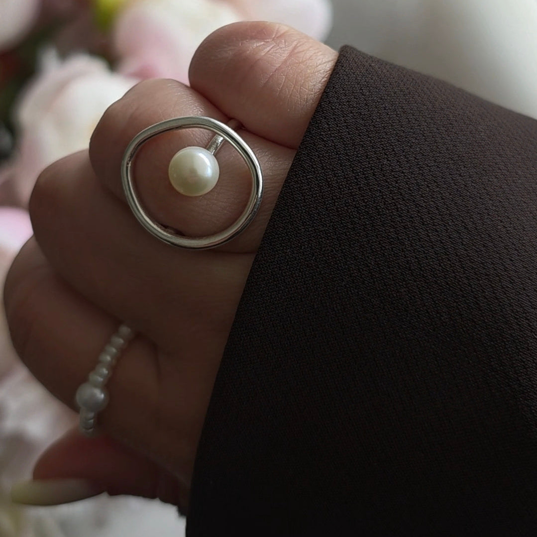 Hand wearing a ring with a pearl on a blurred background
