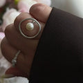 Hand wearing a pearl silver ring and a blazer on a romantic background.
