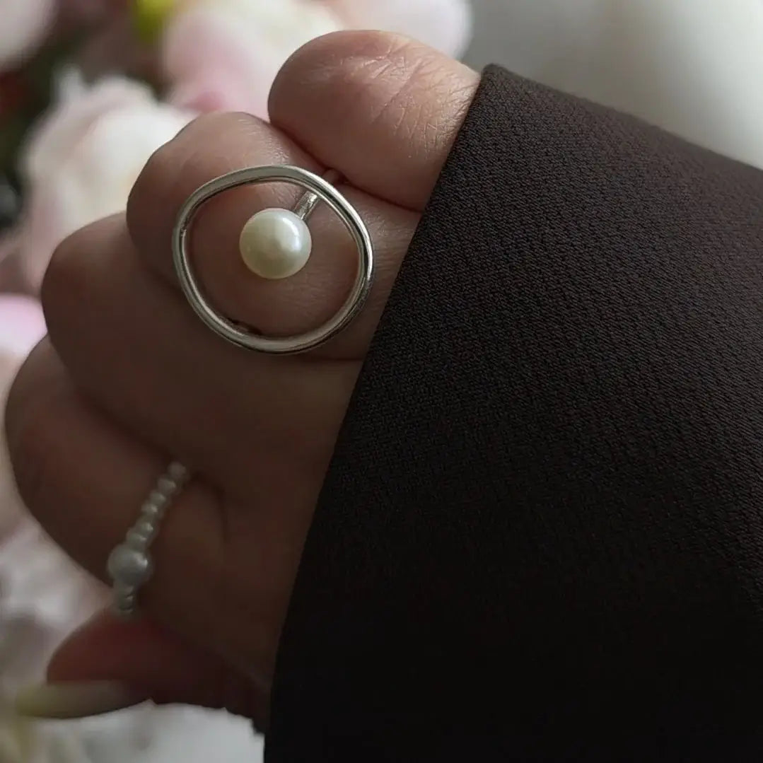 Hand wearing a pearl silver ring and a blazer on a romantic background.