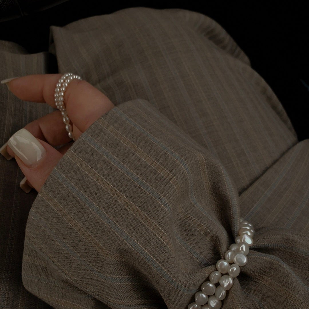 Close-up of a hand wearing a pearl bracelet and midi rings on a dark background