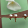Pearl earrings on a stand with a blurred flower in the background