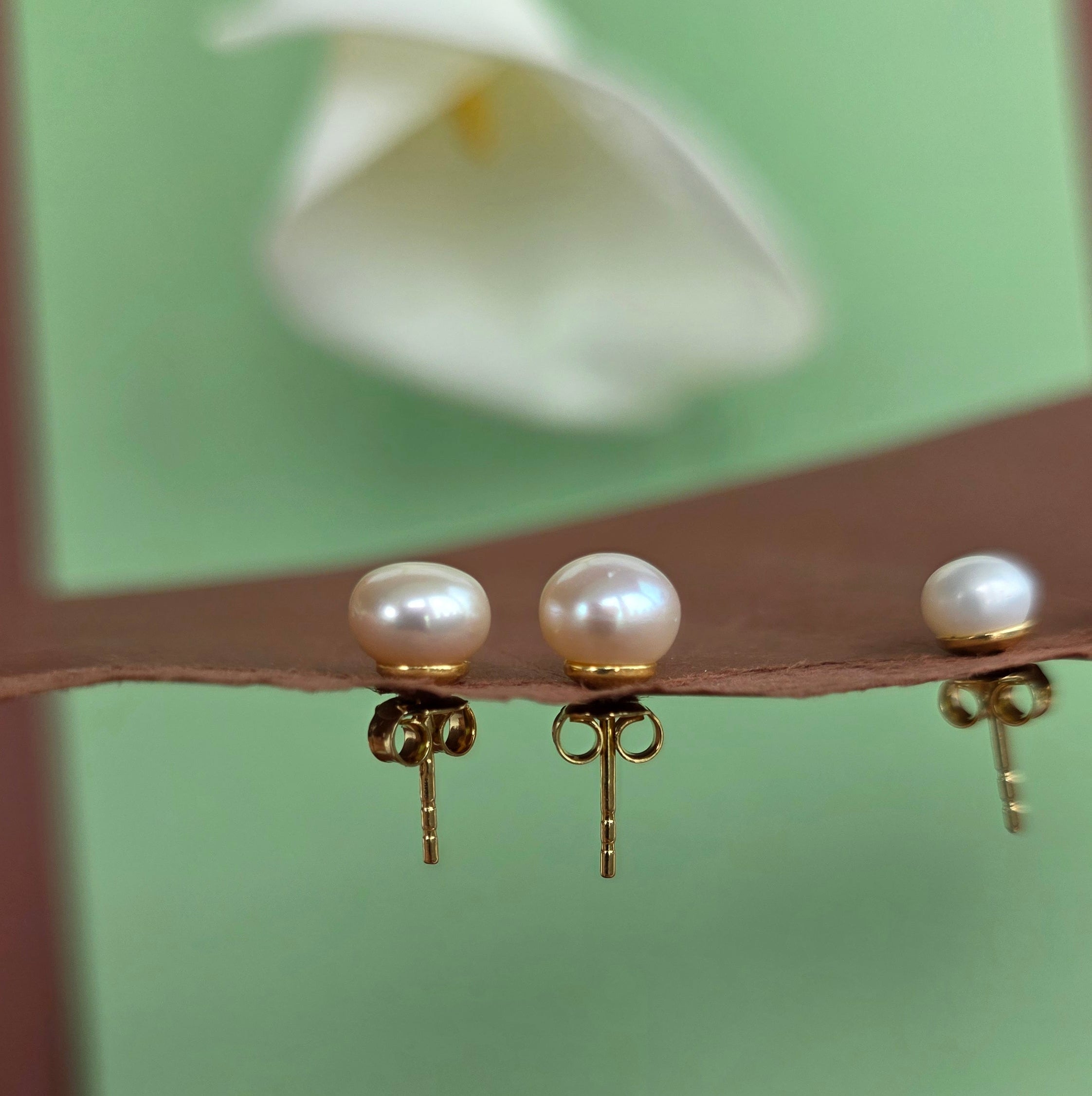 Pearl earrings on a stand with a blurred flower in the background