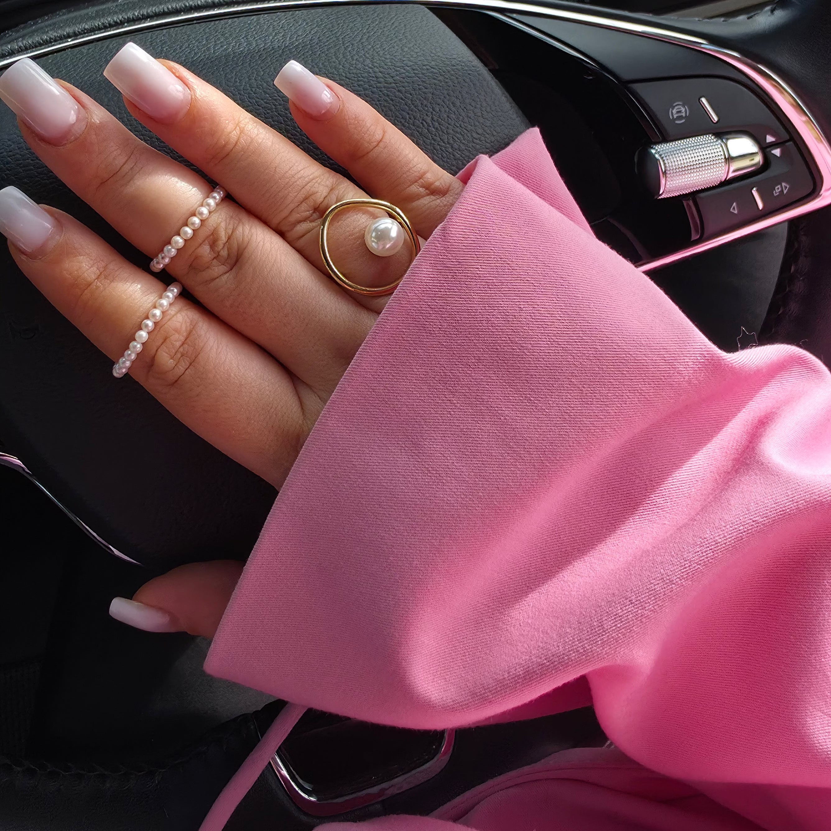 Hand with pink sleeve and pearl rings on car dashboard