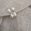 Three baroque pearl stud earrings with gold-tone settings resting on a textured beige linen fabric.