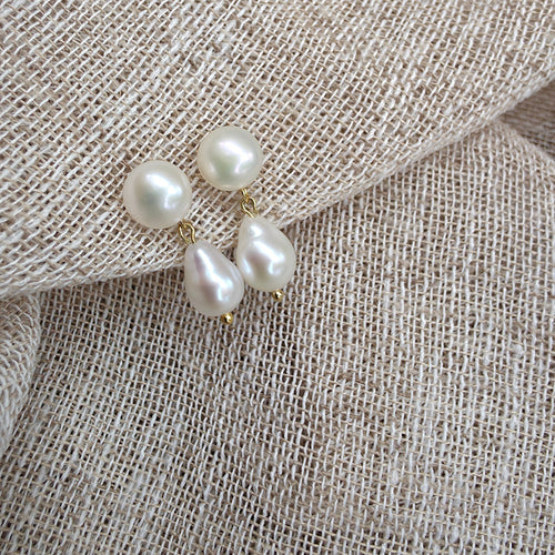 Three baroque pearl stud earrings with gold-tone settings resting on a textured beige linen fabric.
