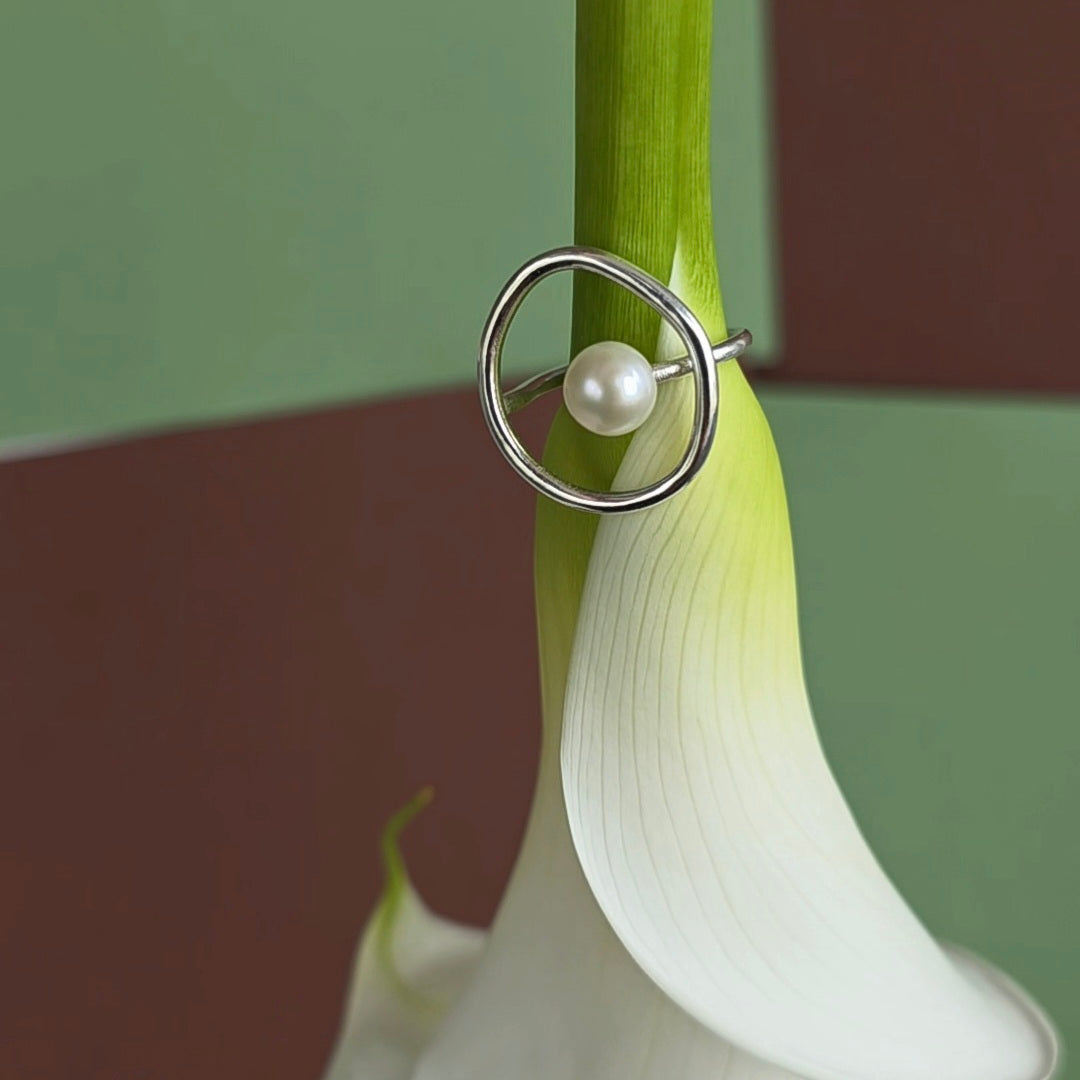 Silver ring with a pearl on a white flower against a green and brown background