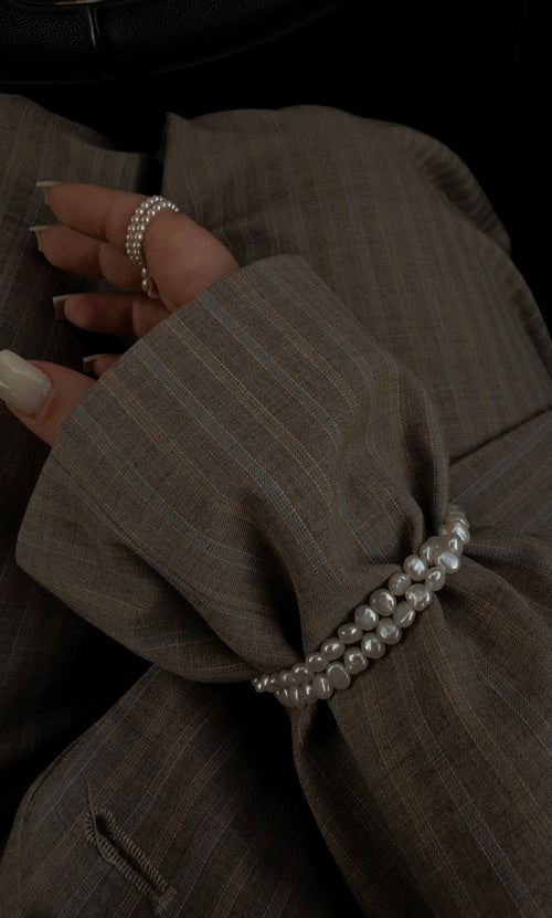 Close-up of a hand wearing a pearl choker as a bracelet on a dark background. 