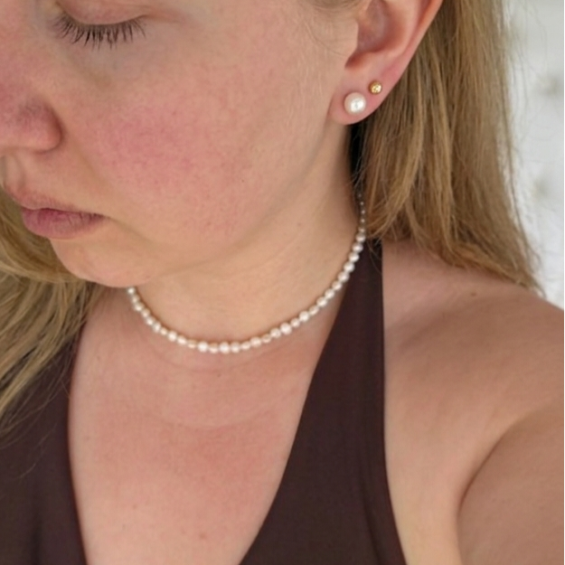 Woman wearing a pearl necklace and earring, looking down.