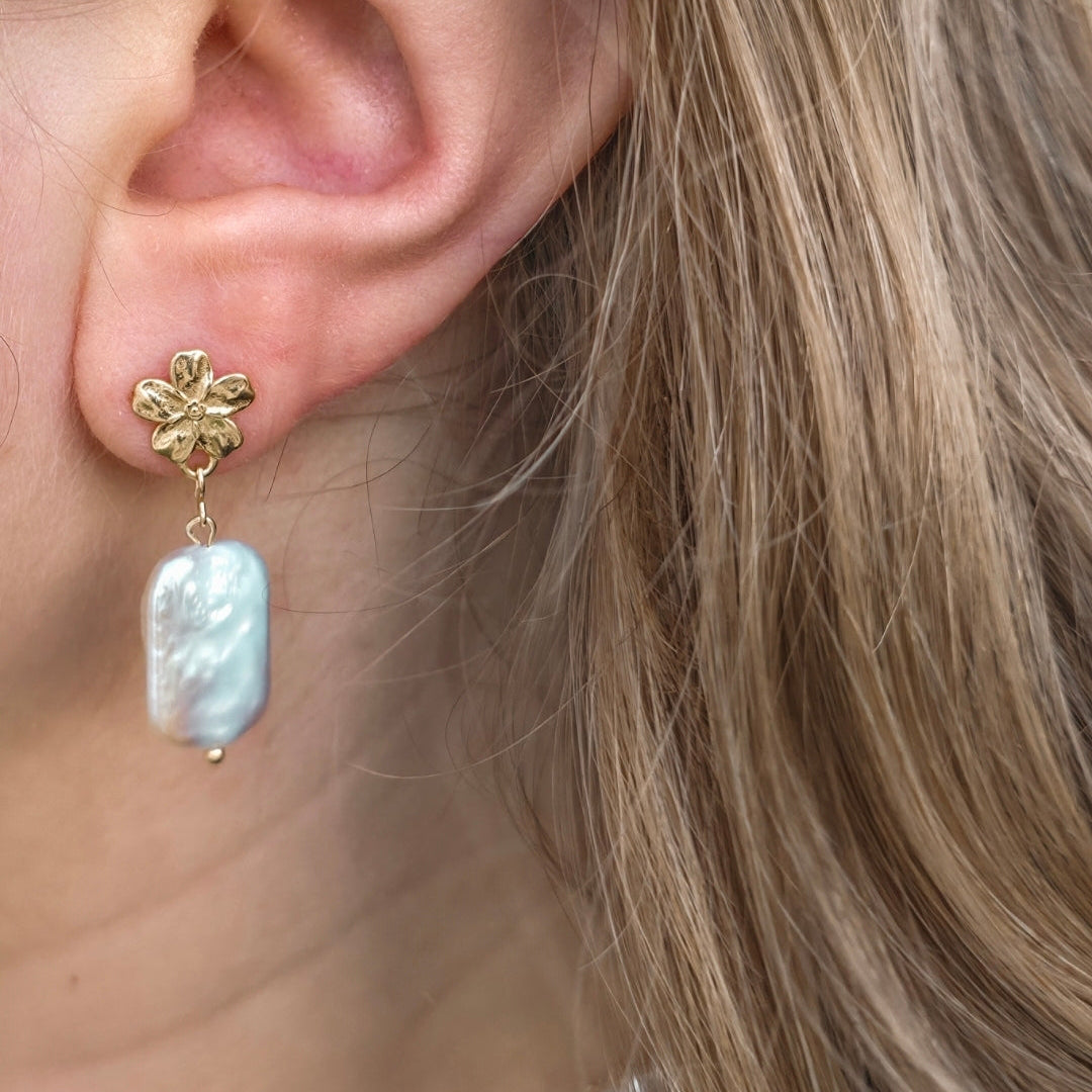 Close-up of an ear wearing a gold earring with a pearl drop.