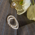 Pearl ring and gold ring on a textured surface with a white flower in the background.