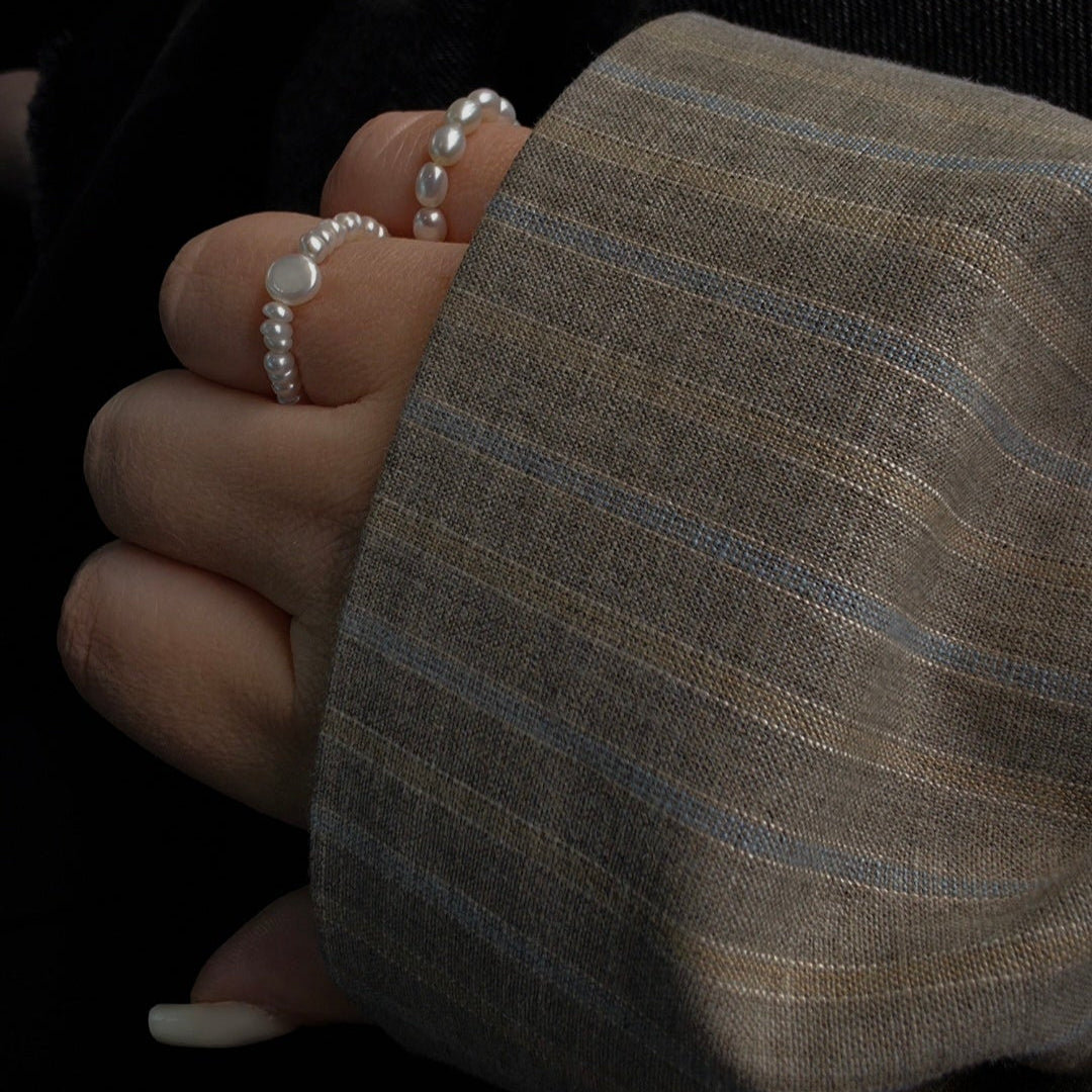 Close-up of a hand wearing two pearl rings with a dark background