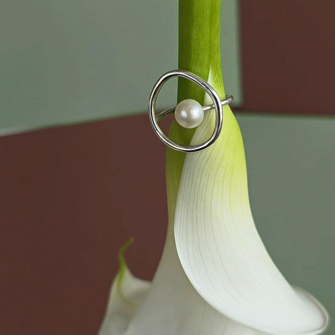 Silver ring with a pearl on a white flower against a gradient background