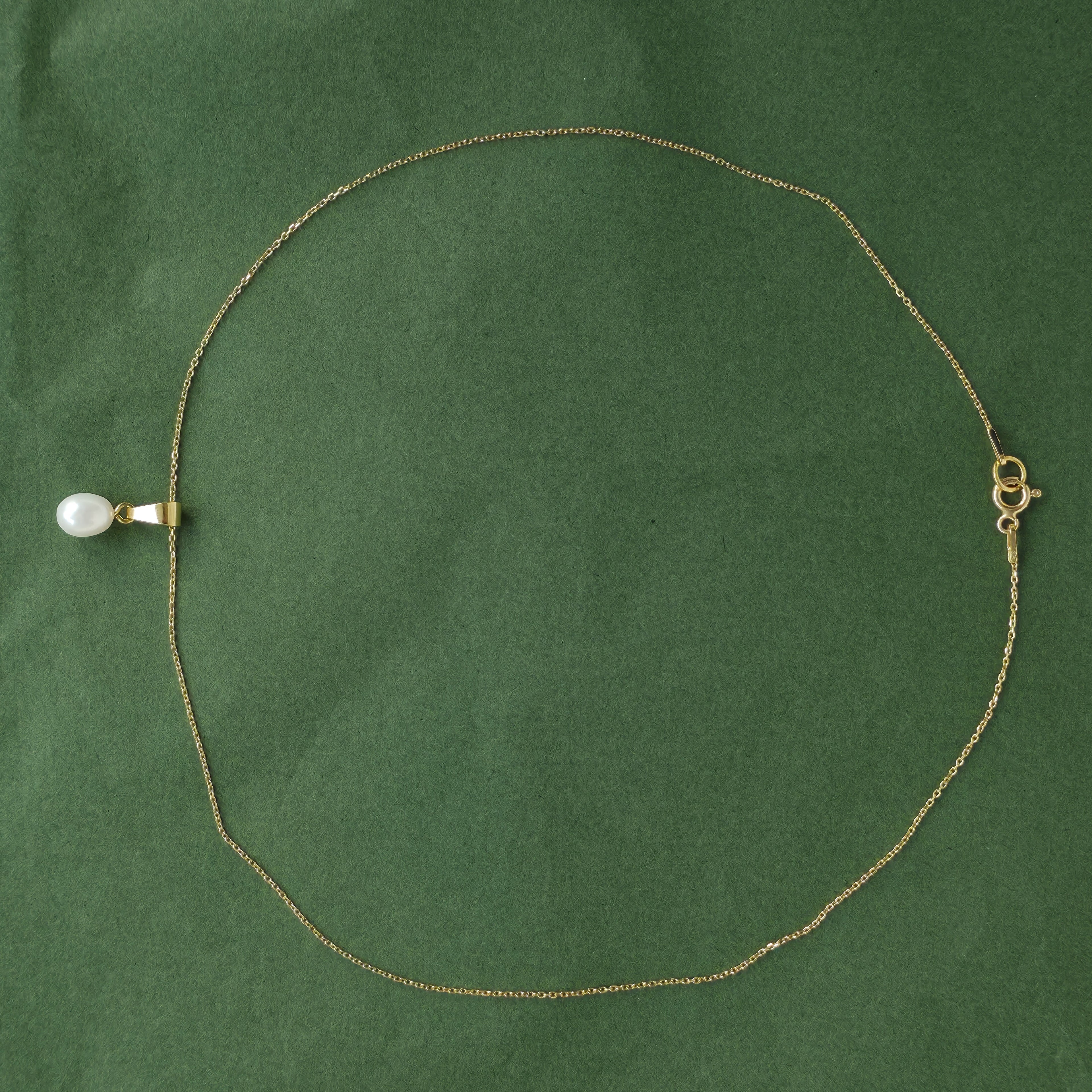 Gold necklace with a white pendant on a green background