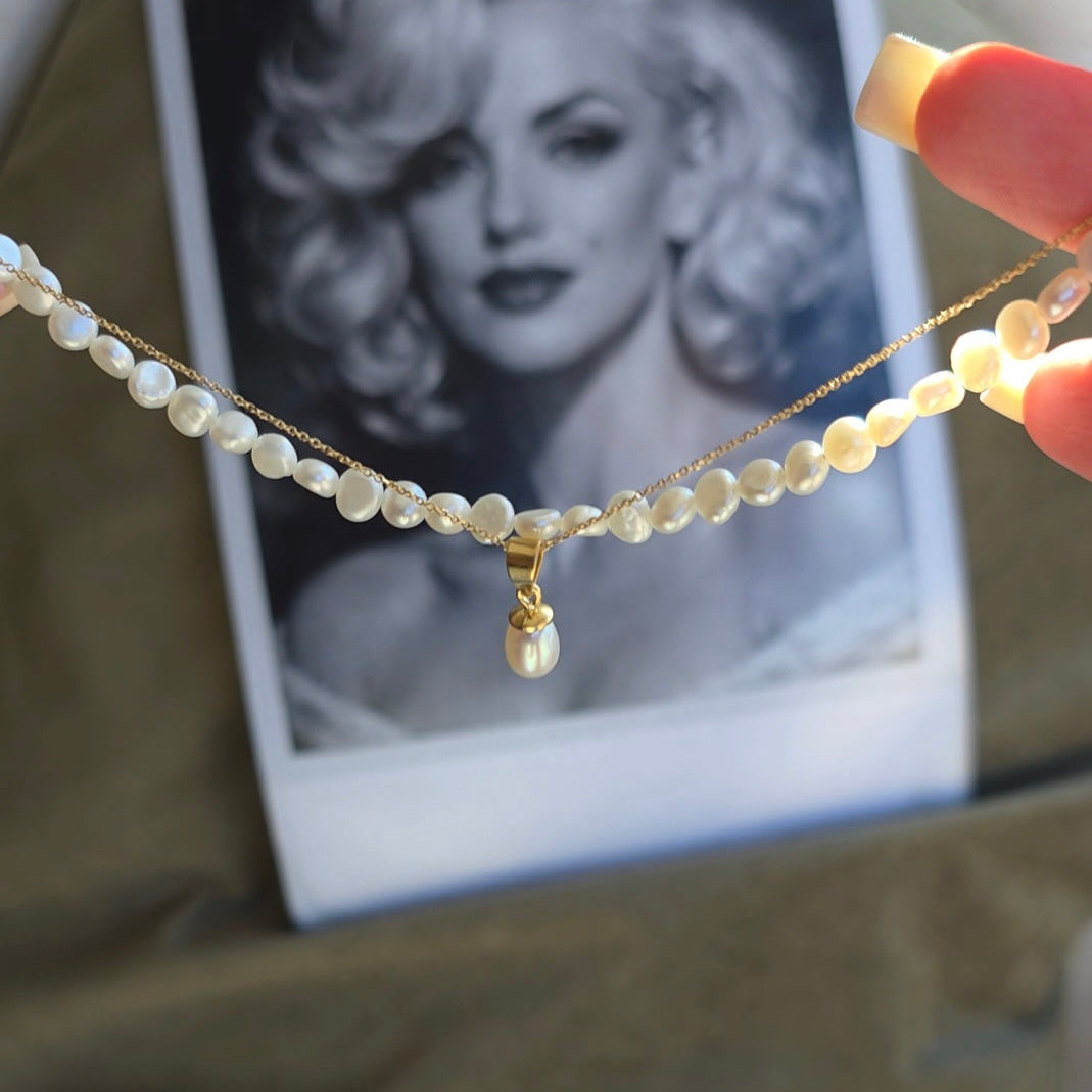 Pearl necklace with a gold pearl pendant held in front of a black and white photo of a famous actress.