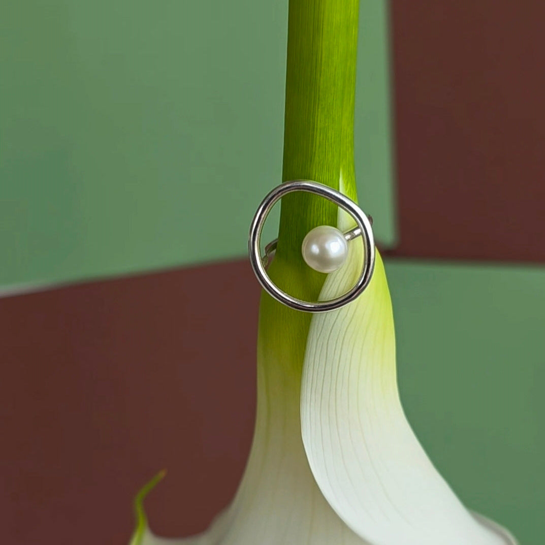 Silver ring with a pearl on a white flower against a green and brown background