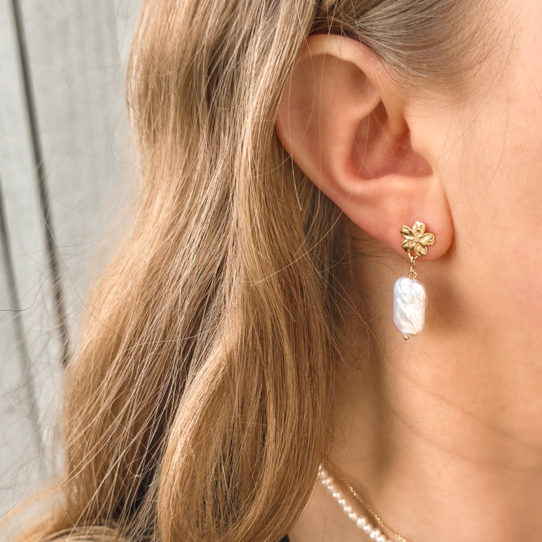 Close-up of a person wearing a pearl earring and necklace with a blurred background