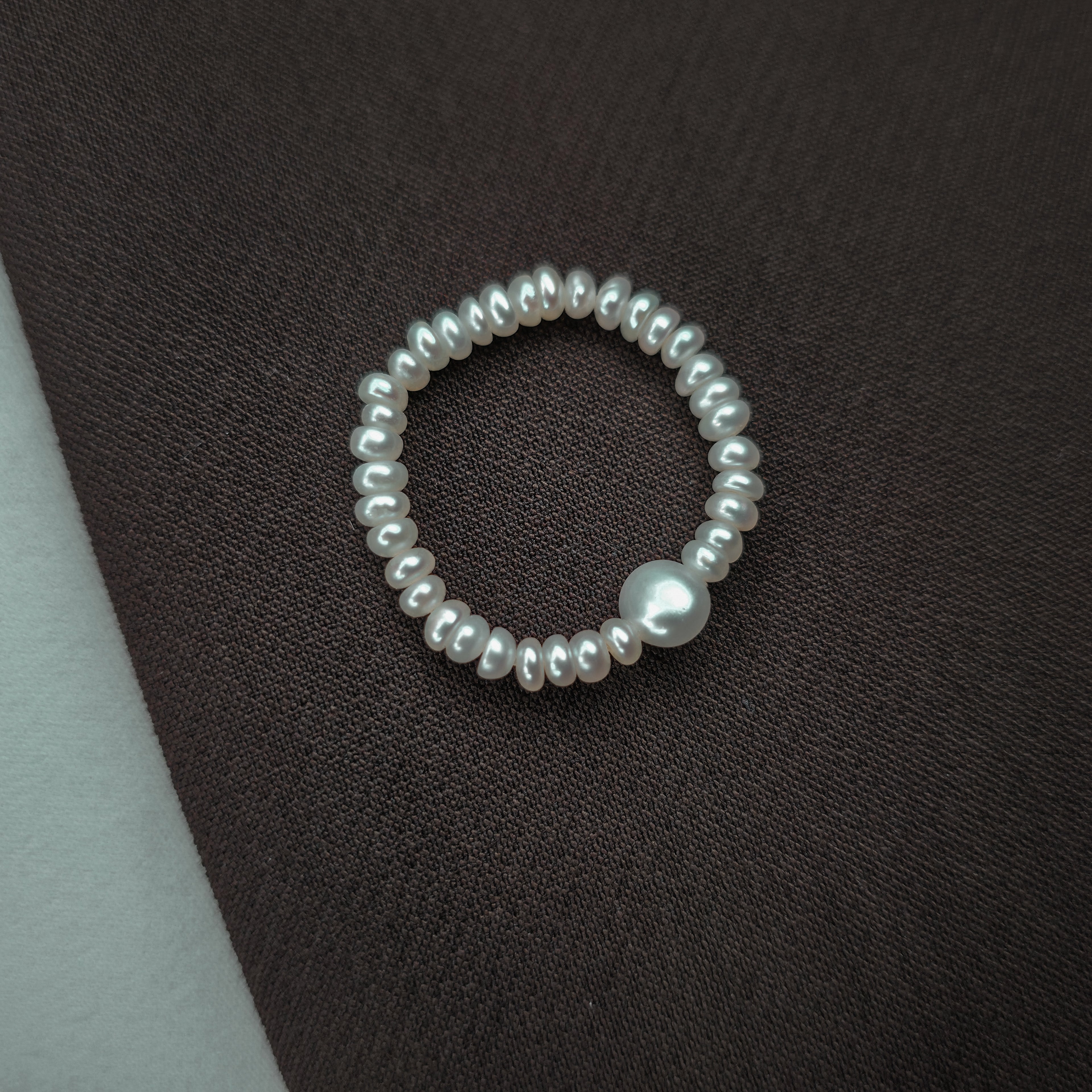 Pearl ring on a textured dark surface.