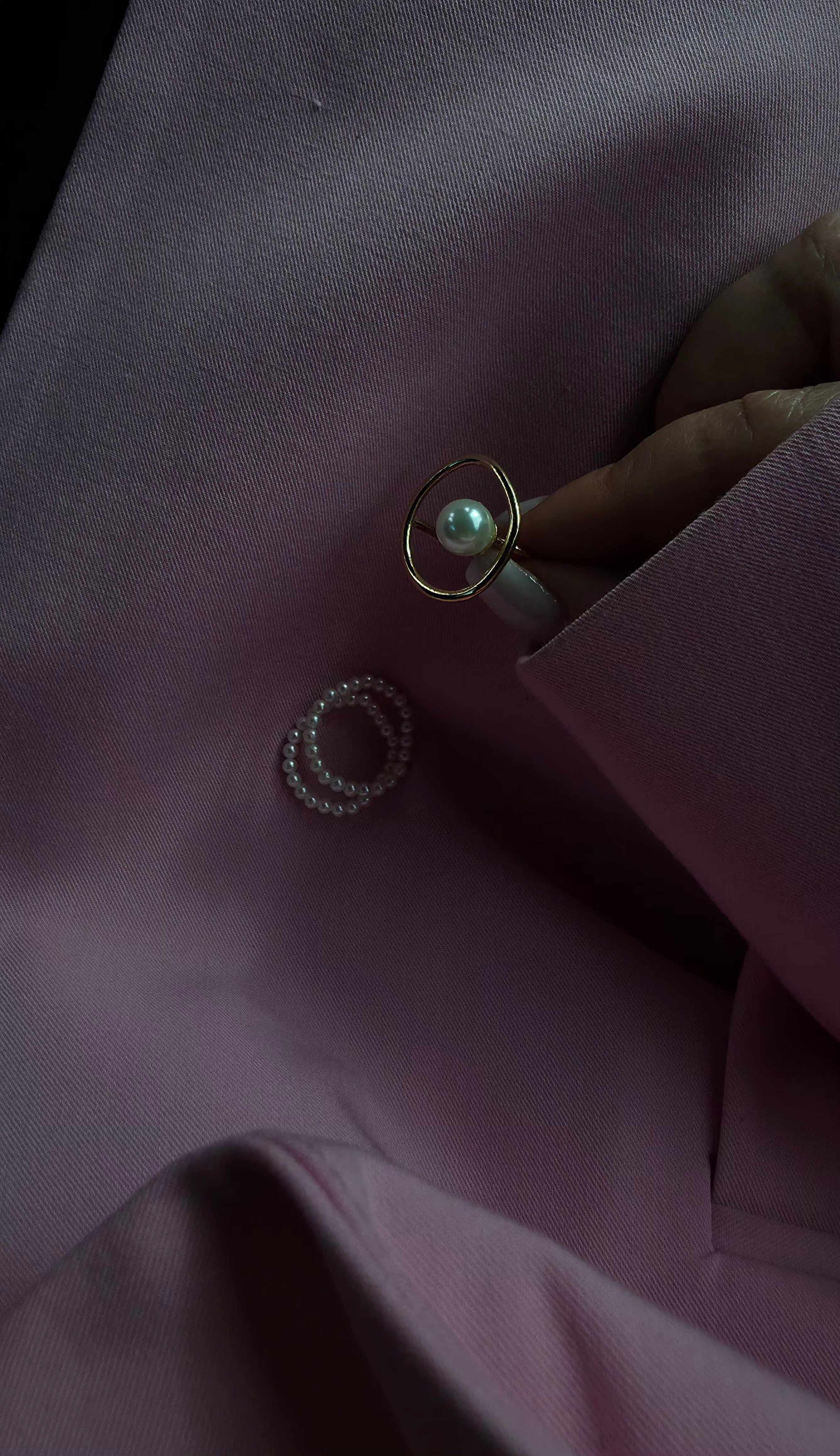 Close-up of a pearl ring on a dark fabric surface placed near a set of pearl midi rings.